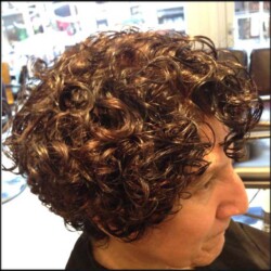 A person with short, curly dark hair sitting in a salon
